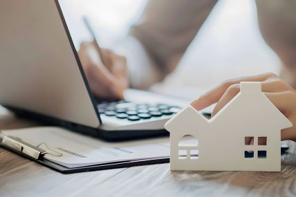 Foto: Person bearbeitet Akten, Modell eines Hauses im Vordergrund